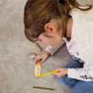 Photographie d'une enfant en train de décorer l'objet en bois qu'elle a fabriqué lors d'une animation consacrée à la préhistoire