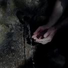 Deux mains jointent récupèrent de l'eau depuis une petit source présente sur un rocher.