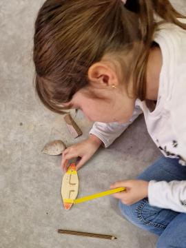 Photographie d'une enfant en train de décorer l'objet en bois qu'elle a fabriqué lors d'une animation consacrée à la préhistoire