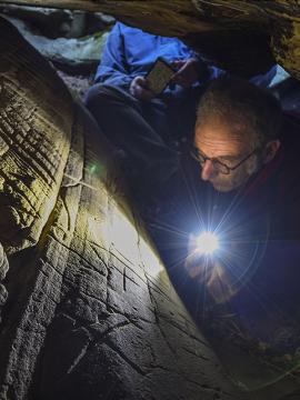 Le chercheur Boris Valentin photographié en train d'observer des gravures préhistoriques dans un abri sous roche 