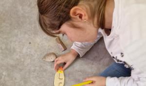 Photographie d'une enfant en train de décorer l'objet en bois qu'elle a fabriqué lors d'une animation consacrée à la préhistoire