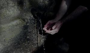 Deux mains jointent récupèrent de l'eau depuis une petit source présente sur un rocher.