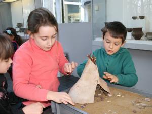 Animation pédagogique consacrée à l'habitat préhistorique. Ici, construction d'une maquette de tente en bois et peau d'animal