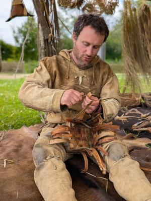 Photographie d'un artisan costumé réalisant une vannerie prothistorique