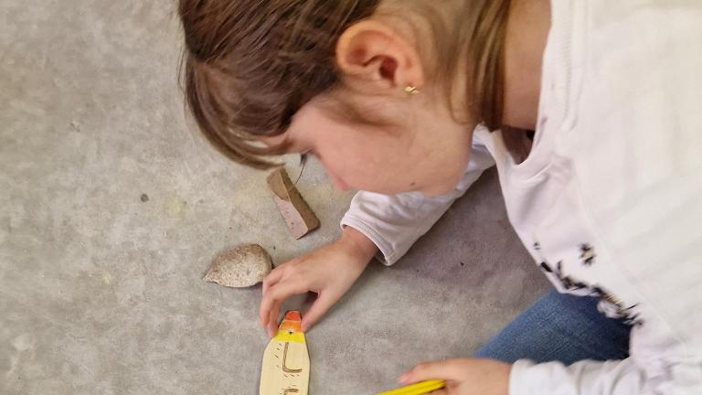 Photographie d'une enfant en train de décorer l'objet en bois qu'elle a fabriqué lors d'une animation consacrée à la préhistoire